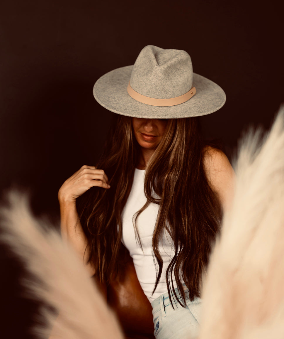 A person with long hair wearing a wide-brimmed hat and a white top, partially obscured by decorative pampas grass.
