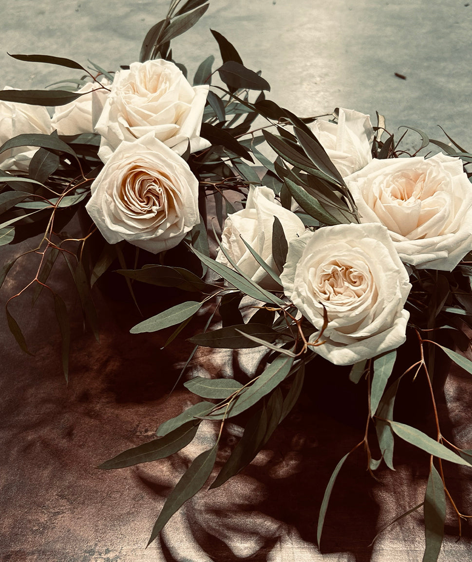 White roses with green eucalyptus leaves arranged on a gray surface.