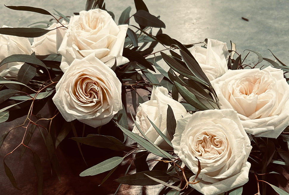 Bouquet of white roses surrounded by green leaves on a wooden surface.