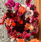 A vibrant bouquet of pink, red, and orange lies artfully arranged on a gravel and wood background, showcasing The Gypsy Dahlia Tubers by Roam & Ivy Flowers for a garden-inspired scene with earthy textures.